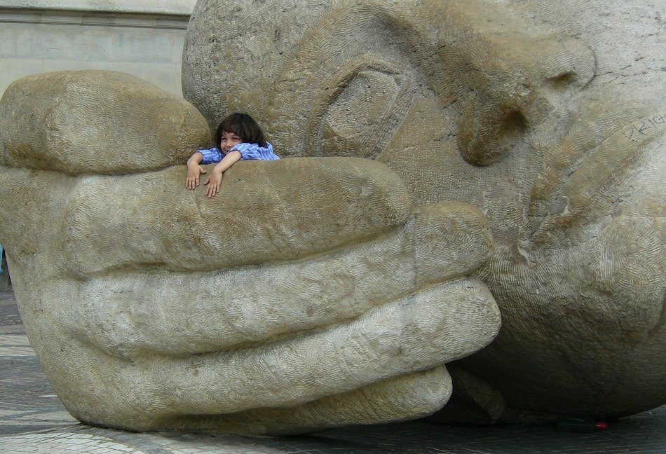 happy child girl on hand of giant stone sculpture, france, paris