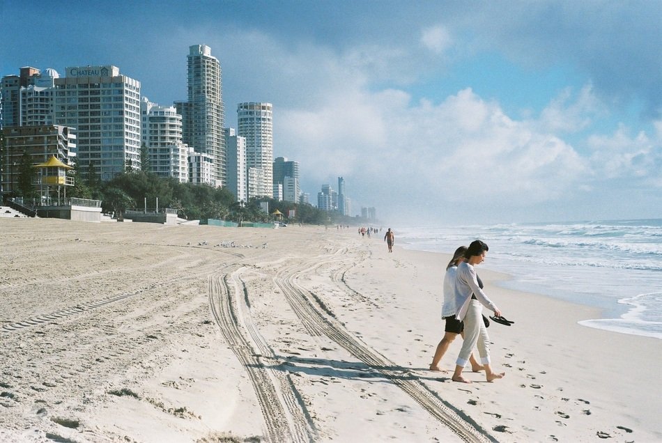 barefoot people walking to water on beach in view of modern city