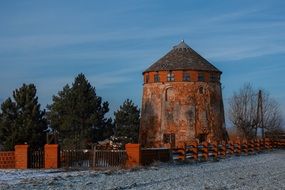 old red windmill in rural winter landscape with plants