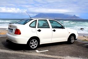 new white vw car parked in view of table mountain at sea, south africa, cape town