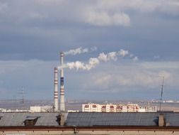 smoking industrial chimneys above long grey roof