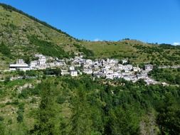 white village buildings on green mountain side under blue sky, italy, liguria