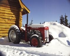 red tractor near log building at snowy winter