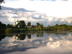 reflection of church in summer countryside on calm water, russia