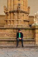 man in hat sits at ancient column in florence in italy