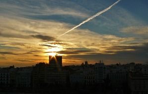 airplane trace across sunset sky above city at dusk