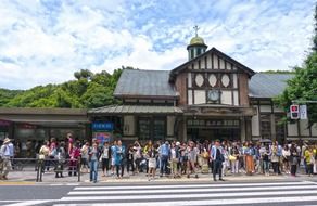 crowd of people at crossing in front of train station building in japan, tokyo, harajuku