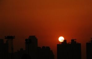 yellow disk of sun at dark red sky above silhouette of city