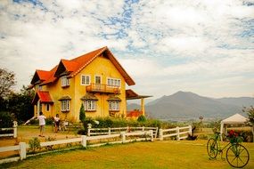 young boy and girl at fenced yellow house in beautiful landscape