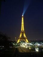 illuminated eiffel tower with beams of blue light and yellow lights at night sky in city, france, paris