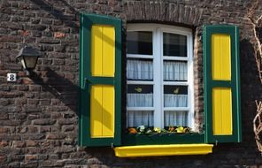 window with yellow and green shutters on old brown brick facade