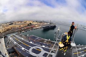 man working on mast in view of uss carl vinson Nimitz-class supercarrier at harbour in usa, california, san diego