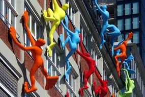 colorful human figures climbing facade of grey building, germany, düsseldorf