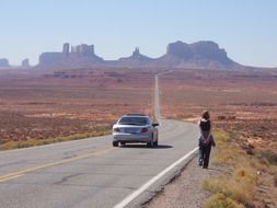 car and walking woman on road to monument valley rock formations, usa, utah, arizona