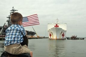 child boy with american flag on harbour in view of hospital-ship, usa, virginia, norfolk