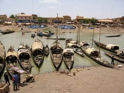 people and traditional wooden boats on shoreline, mali