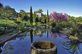 spring garden and old village houses mirroring on water, france