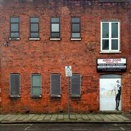 young man in glasses, graffiti on door in red brick facade