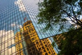 reflection of tall building with american flag atop on glass facade