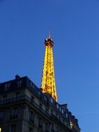 illuminated top of eiffel tower behing building at dusk, france, paris