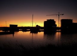 tower crane and buildings under construction in harbor at sunset