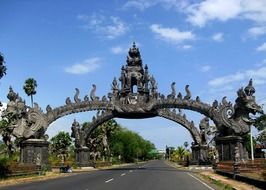 ancient arch with carved stone dragons above road, indonesia, bali, gilimanuk