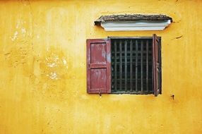 window with shutters and cage on a yellow wall