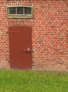 locked wooden door and grated small window on red brick facade