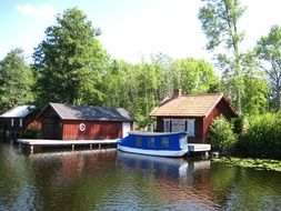 boat houses and covered boat at pier on forest lake, sweden, gota channel