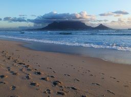 footprints on beach in view of table mountain under clouds, south africa, cape town