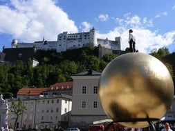 person at top of golden sphere in view of city and hohensalzburg fortress, austria, salzburg