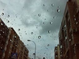 cloudy sky and city through glass with rain drops