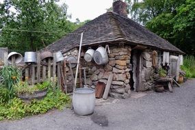 Rural stone cottage with utensils on a fence among the plants