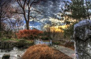 stone footbridge across stream in arboretum at autumn sunset