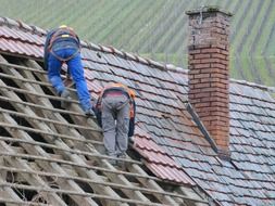 two workers tear off tiles on roof of old house