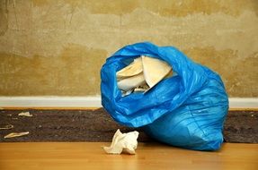 blue bag with garbage on floor at wall