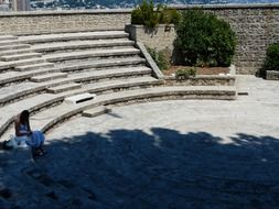 lonely woman sits on stone bench in open air theatre, monaco, fort antoine