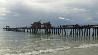 people on long wooden pier on sea at cloudy weather, usa, florida