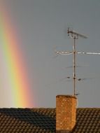 rainbow in grey sky at tile roof with chimney and antenna