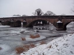 old stone bridge across frozen river in countryside