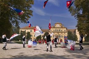 boys and girls in historic costumes twirling flags in front of old building in italy, parma