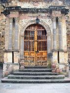 aged arched wooden door in grunge stone wall, mexico