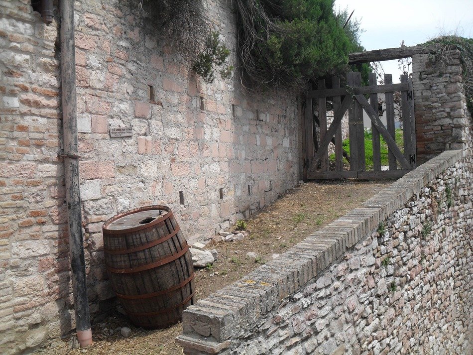 barrel at old brick wall before gate, italy, assisi