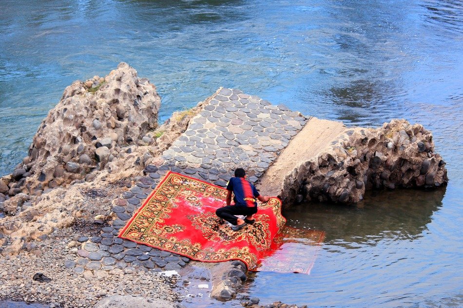 man washing carpet on rock at water