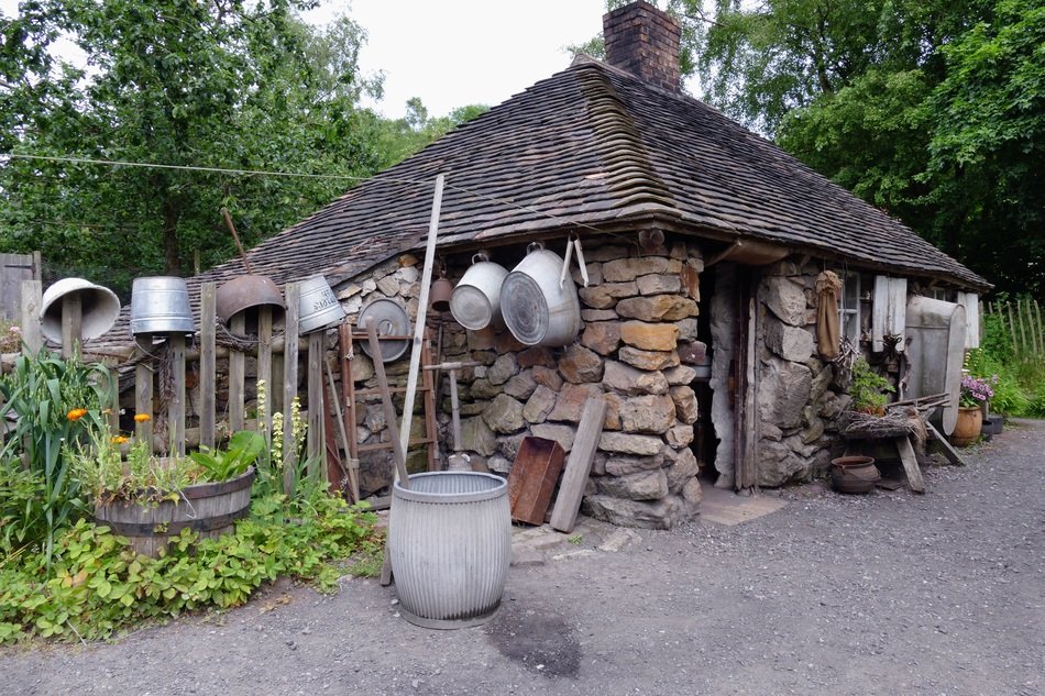 Rural stone cottage with utensils on a fence among the plants