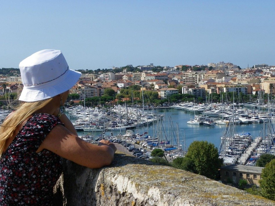 girl in hat looking on boats in bay at town, france, antibes