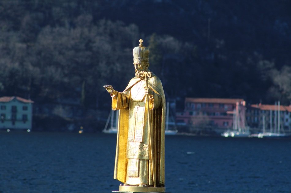 golden Saint Nicholas statue in view of coastal town, italy, lecco