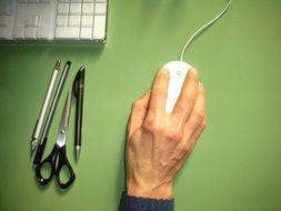 male hand on mouse, keyboard and office supplies on green desk