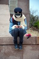 person with mask in the cap looks in a smartphone