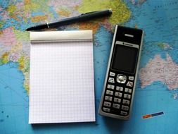 mobile phone, pen and blocknote on map of the world